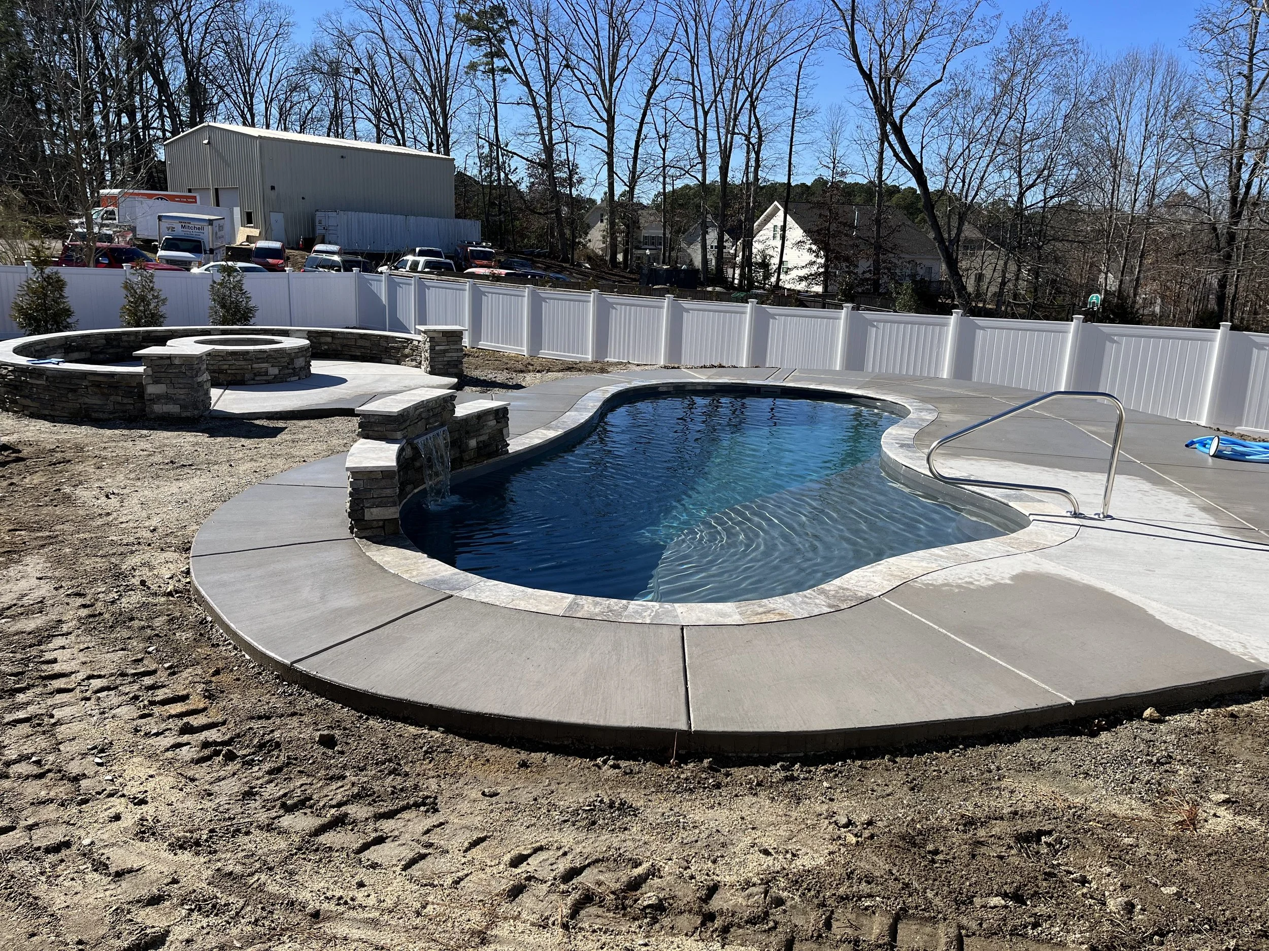 Fiberglass in-ground pool with splash pad and finished concrete deck