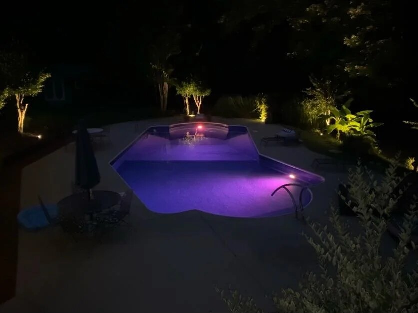 In-ground pool and patio at night with landscape lighting